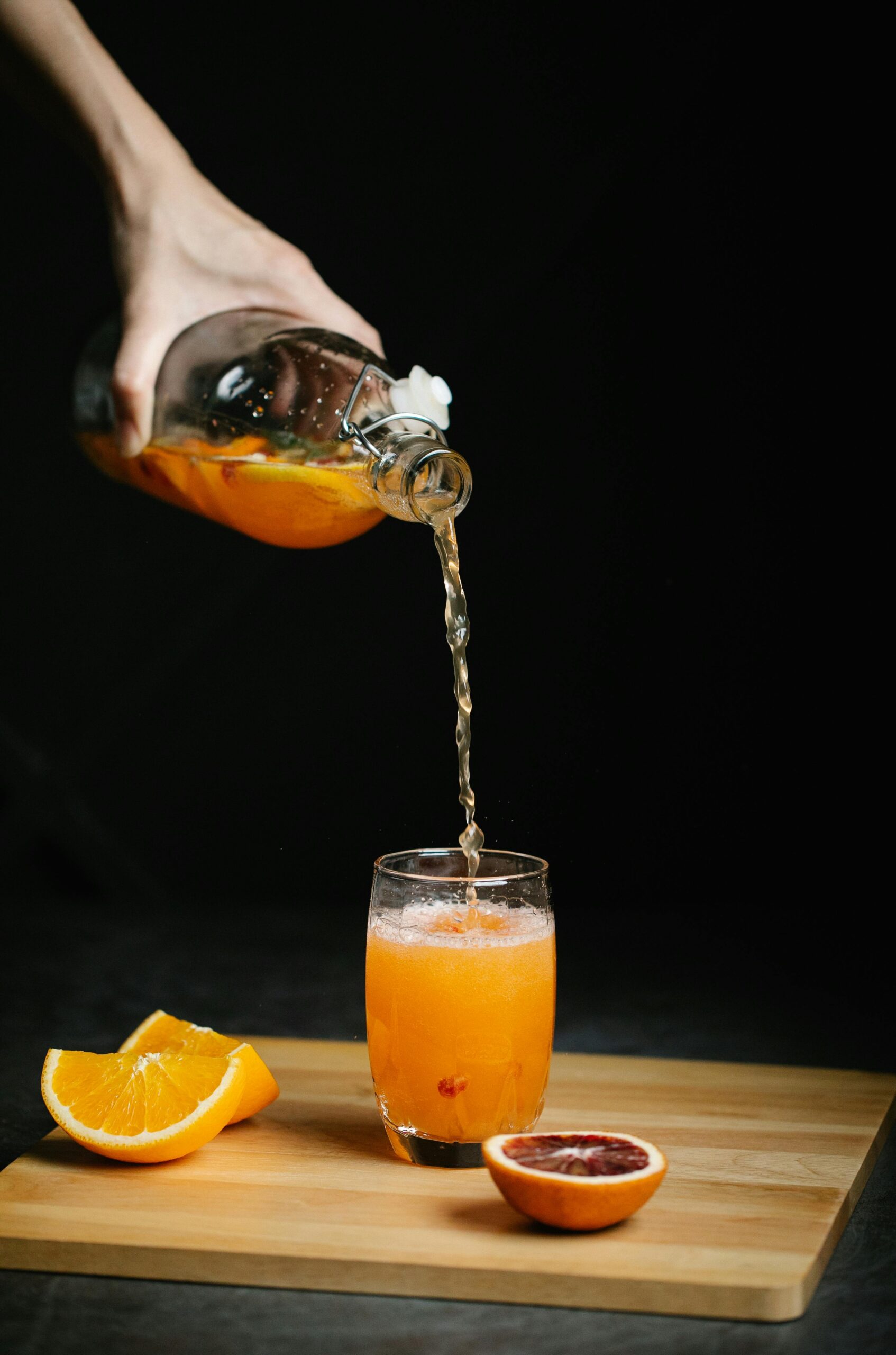 Fresh orange juice being poured into a glass on a wooden board, with oranges nearby.